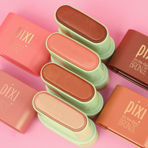 Six Pixi On-the-Glow Bronze face powders in various warm shades, arranged vertically in the center with their coral-pink and terracotta-colored rectangular boxes on a solid pink background. view 2