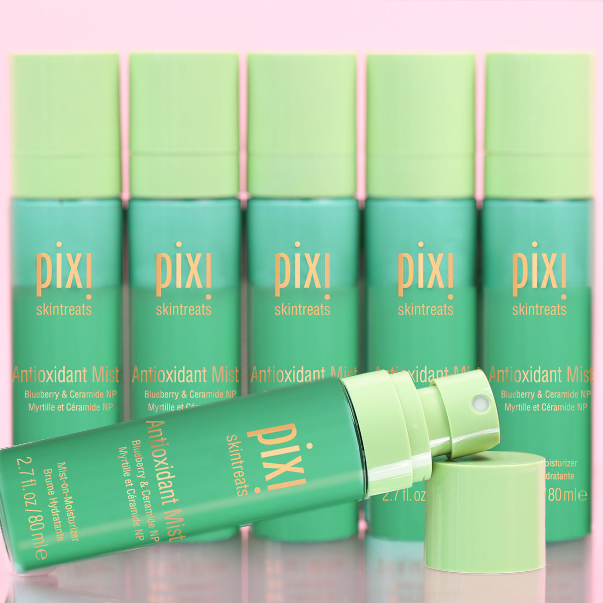 Six Pixi Skintreats Antioxidant Mist bottles in a teal and light green color scheme, with one bottle lying open in the foreground and its cap beside it, set against a soft pink background.