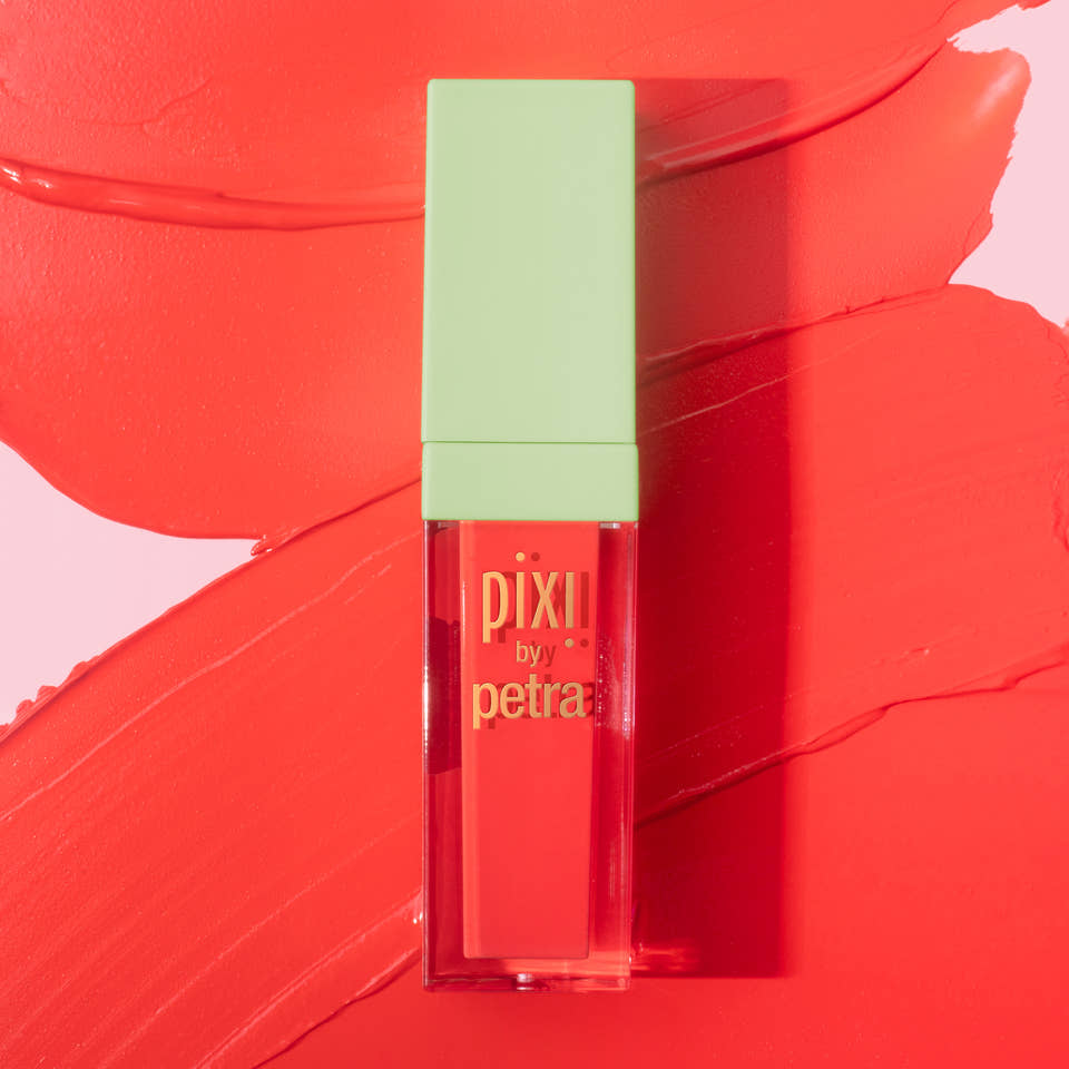 Pixii by Petra liquid lipstick in a clear rectangular tube with a light green cap, set against a vibrant coral-red background with a matching lipstick smear. view 1